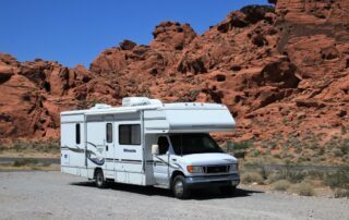 A white rv parked in front of a red rock formation.