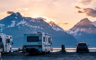 A group of rv's parked in front of a lake with mountains in the background.