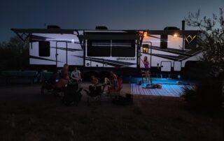 A group of people sitting around an rv at night.
