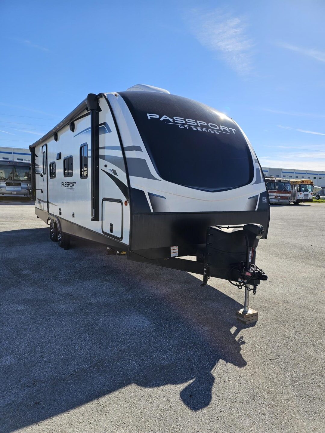 A modern passport travel trailer parked in a lot on a sunny day, featuring a sleek black and gray design with prominent branding.