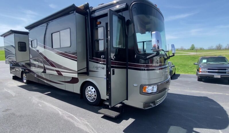 Large luxury motorhome with a curved windshield, extended side slide-out, and open entry door with stairs, parked on a lot.